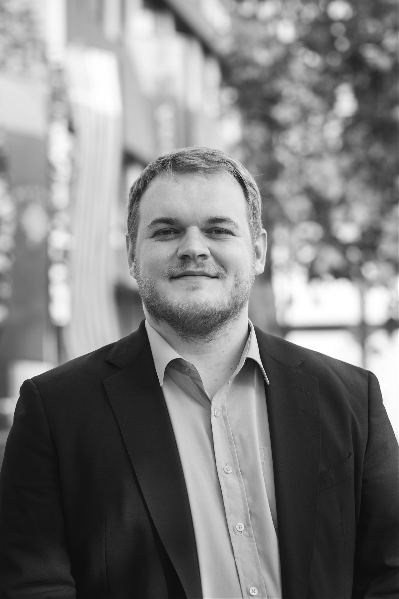 Black and white portrait of a person in a suit smiling outdoors.